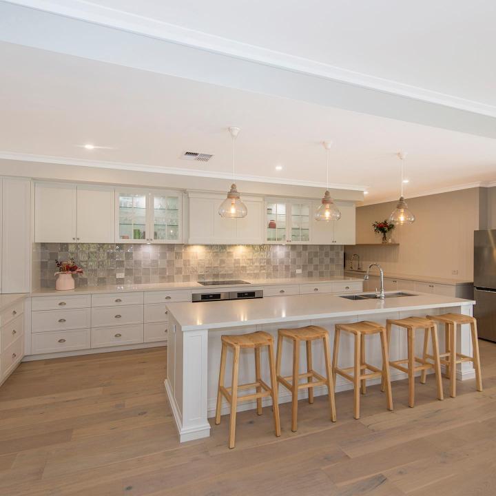 Modern white kitchen with a large island and wooden bar stools.