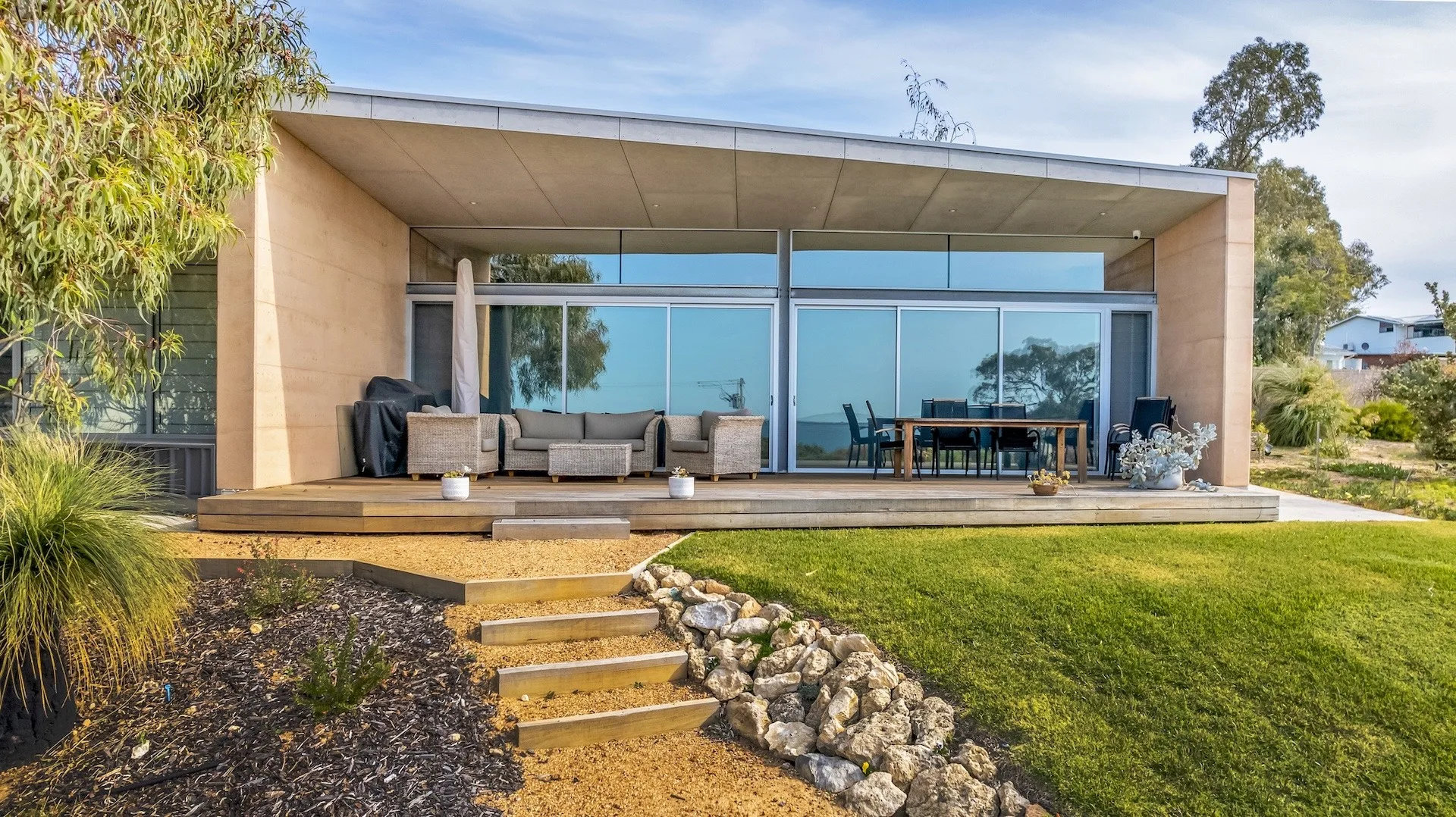 Modern single-storey home in Dawesville with full-height glazing, a covered alfresco area and timber decking, set against landscaped coastal gardens