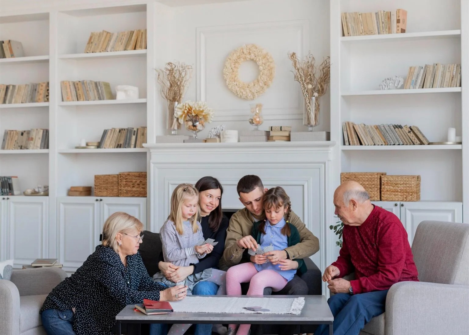 A multi-generational family relaxing together in a living room with built-in shelving and a neutral farmhouse palette